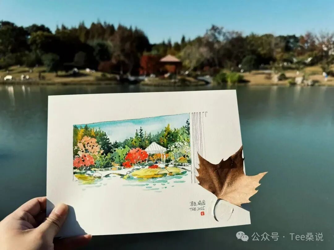 手持湖边亭子与树林的水彩写生,背景是现场湖景